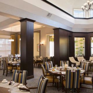 A spacious and elegantly designed restaurant dining area with several tables and chairs, illuminated by chandeliers.