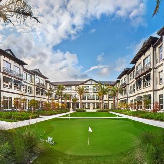 A luxurious resort with beautiful gardens and a putting green under a bright, partly cloudy sky.