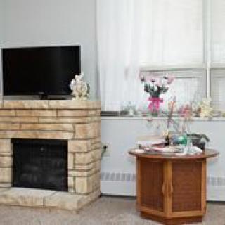 A cozy living room featuring a stone fireplace, a television mounted above, and a wooden table with various decorations.
