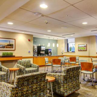 A modern and comfortable waiting area with chairs and tables, adorned with artwork and well-lit surroundings.