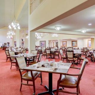 A spacious restaurant dining area with neatly arranged tables and chairs, featuring elegant lighting and a carpeted floor.