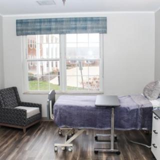 A clean and simple hospital room with a bed, chair, and window.