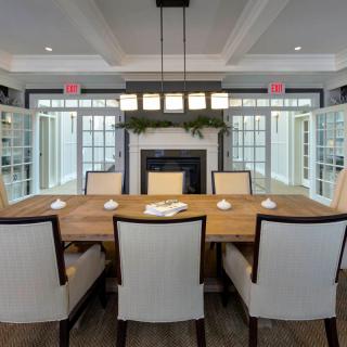A stylish dining room with a wooden table and upholstered chairs, framed by large windows and a central fireplace.