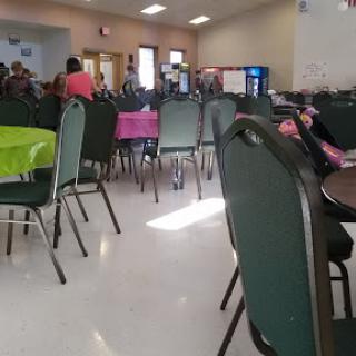 A view of a community gathering area filled with chairs and tables, where people are mingling.