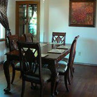 A dining room with a wooden table and chairs, featuring a decorative painting on the wall.