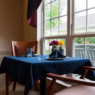 A cozy dining setup with a blue tablecloth and flowers by a large window.