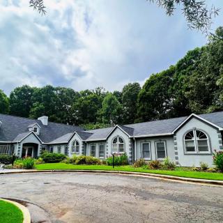 A beautiful single-story house with a well-maintained garden and a circular driveway surrounded by lush trees.