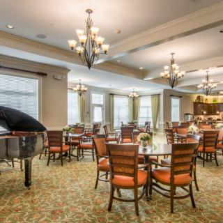 A spacious dining area with elegant chandeliers, a grand piano, and neatly arranged tables and chairs.