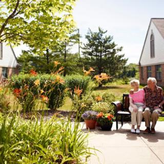 A cheerful elderly couple enjoying a sunny day in their garden, surrounded by vibrant flowers and greenery.