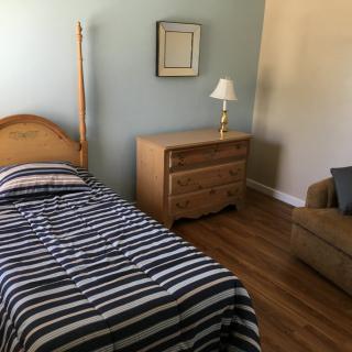 A minimalist bedroom with a single bed, striped bedding, and wooden furniture.