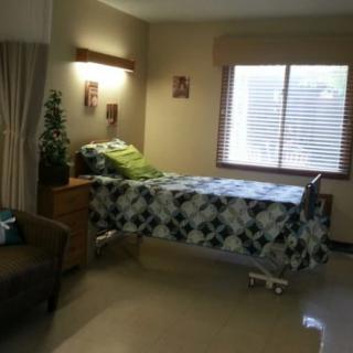 A hospital room with a single bed, green bedding, and a window with blinds.