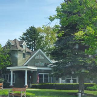 A picturesque house surrounded by lush greenery and trees, with benches in the front yard.