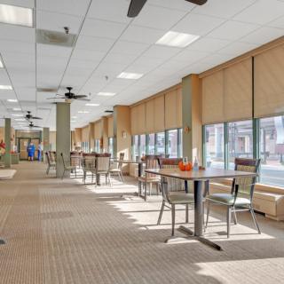 Spacious dining area with tables and chairs, featuring large windows and blinds.