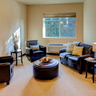 A cozy living room with comfortable armchairs and a round coffee table, illuminated by natural light from the window.