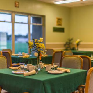 A cozy dining area set with green tablecloths, elegant place settings, and floral centerpieces, creating a warm atmosphere for guests.