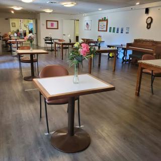 A neatly arranged dining room with tables, chairs, and a vase of flowers, featuring a piano in the corner.