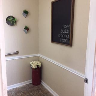 A small bathroom corner featuring a chalkboard, wall-mounted plants, and a vase with flowers.