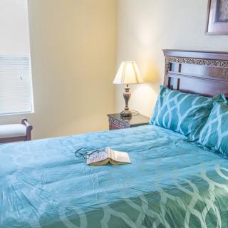 A cozy bedroom featuring a neatly made bed with teal bedding, a bedside lamp, and an open book.