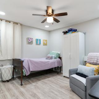 A cozy and well-lit bedroom featuring a ceiling fan, a neatly made bed, and simple yet stylish decor.