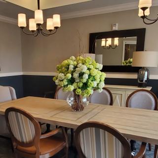 A elegantly designed dining room featuring a large table with a floral centerpiece, surrounded by chairs, and illuminated by a chandelier.