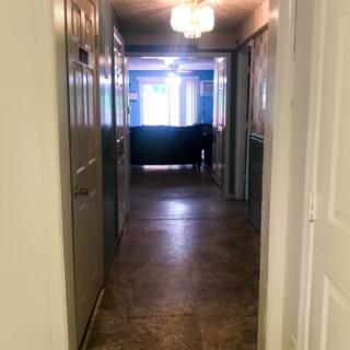A hallway with a chandelier, leading to a brightly lit room.