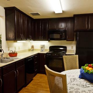 A modern kitchen with dark cabinets, featuring a dining area and a fruit basket on the table.