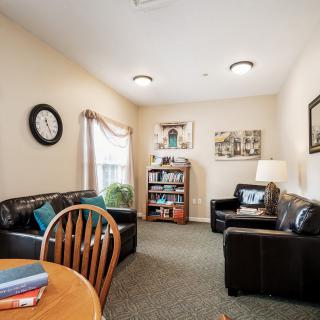 A cozy living room featuring two sofas, a bookshelf, a table with chairs, and decorative elements such as a clock and wall art.