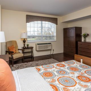 A cozy bedroom with a patterned bedspread, wooden furniture, and a large window allowing natural light.