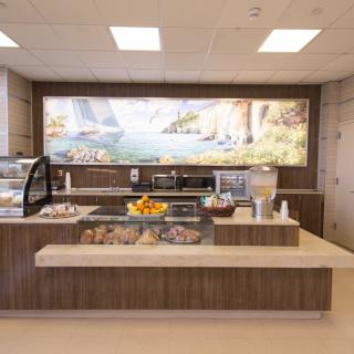 A modern cafe interior with a dessert and drink counter, featuring a scenic mural on the wall.