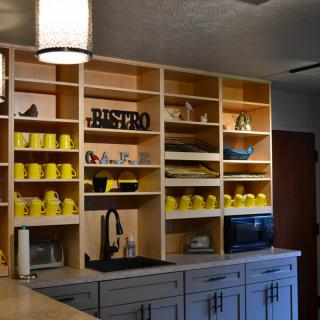 A cozy kitchen area with open shelves displaying yellow mugs and a bistro sign.