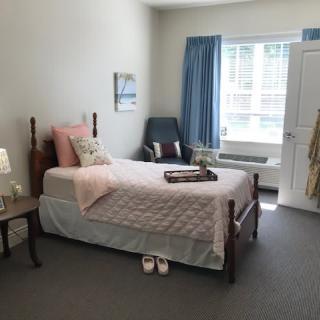 A cozy bedroom with a single bed, decorated with soft pink accents and illuminated by natural light.