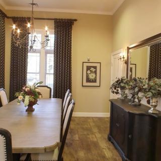 A well-decorated dining room featuring a long table, elegant chandelier, and large curtains.