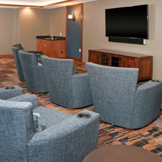 A cozy theater room with cushioned lounge chairs arranged in rows facing a large flat-screen TV.