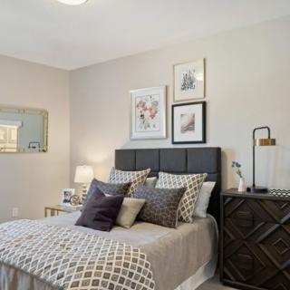 A modern and stylish bedroom interior with a neatly made bed, decorative pillows, wall art, and bedside tables with lamps.