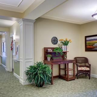 A neatly decorated hallway with a small desk, chair, and potted plants.