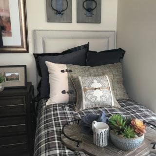 A cozy bedroom with patterned bedding, decorative pillows, and a tray on the bed holding a succulent and a mug.