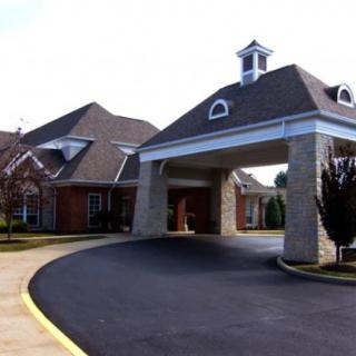 A building with a covered entrance and driveway, featuring stonework and a sloped roof.