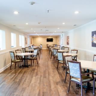 An empty dining room with wooden floors and arranged tables and chairs.