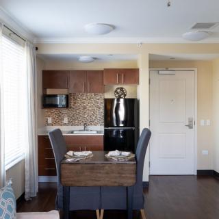 A modern kitchen and dining area in an apartment, featuring a table set for four, with a fridge and microwave in the background.
