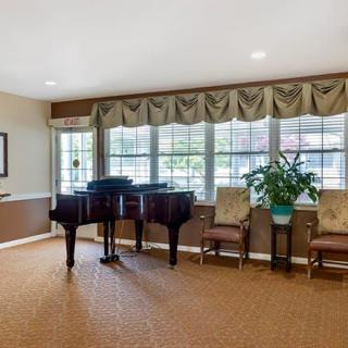 A cozy room featuring a grand piano, chairs, and large windows with drapes.