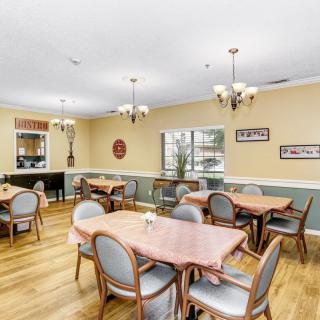 A cozy dining room with multiple tables and chairs, featuring chandeliers and wooden flooring.