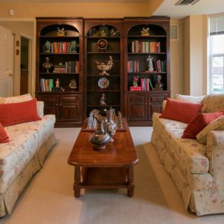 A cozy living room featuring two sofas with red cushions, a wooden coffee table, and bookshelves filled with books and decorations.