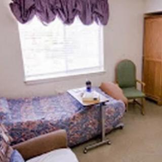 A small room with a single bed, window, chair, and tray table.