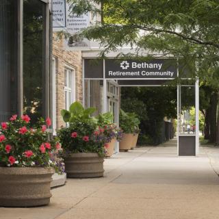 A sidewalk adorned with colorful potted flowers and trees, leading to a building entrance.