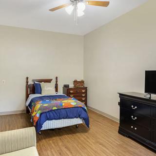 A minimalist bedroom with a single bed, television, and dresser on a wooden floor.