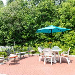 A sunny outdoor patio with a table, chairs, and an umbrella surrounded by lush greenery.