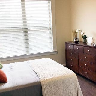 A cozy bedroom with a neatly made bed and a wooden dresser near a large window.
