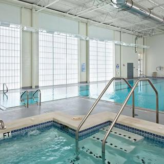 An indoor swimming area with a large pool and adjacent jacuzzi, surrounded by tall windows.