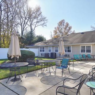 A sunny patio area with chairs, tables, and umbrellas outside a building.
