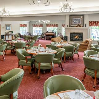 A cozy dining room with neatly arranged tables and chairs, featuring a warm fireplace and elegant chandeliers.